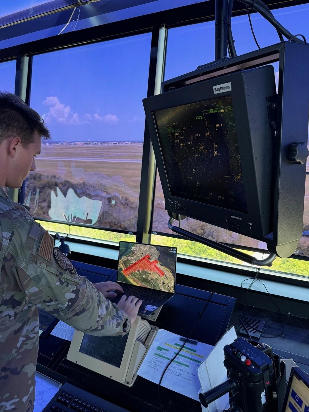A man in military fatigues standing at a domain airspace awareness terminal looking at volumes and aircraft tracks on maps
